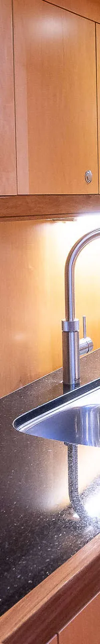 Een kombuis met een donker aanrechtblad, een dubbele spoelbak, een kraan, een kookplaat, een oven en houten kasten.