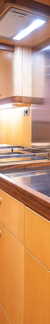 Een kombuis met houten kasten, een donker aanrechtblad, een kookplaat, een oven en een espressomachine.