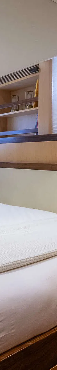 Een slaapkamer met een tweepersoonsbed, twee kussens, een deken, houten kasten en een rieten tas.