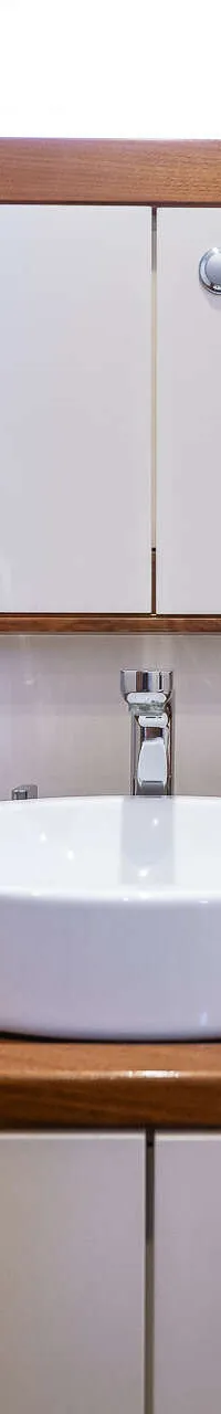 Een badkamer met een witte wasbak, een kraan, een spiegelkastje en een houten aanrechtblad.