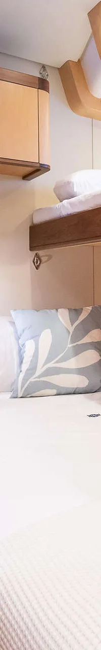 Een kajuit met een tweepersoonsbed, een stapelbed erboven, houten kasten en een laptop op het bed.