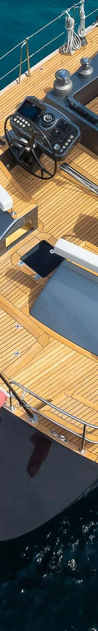Een bovenaanzicht van een zeiljacht met een houten dek en een uitgeklapt zwemplatform, omringd door helderblauw water.