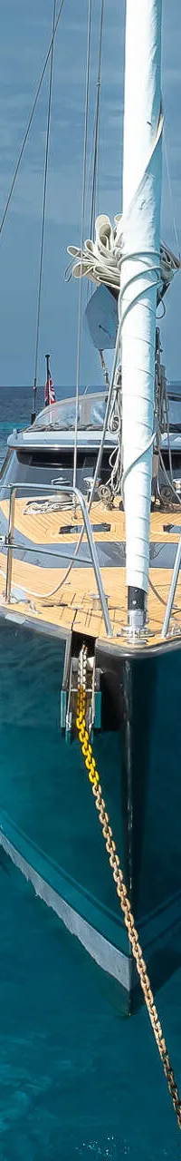 Een zeilboot met een donkere romp en een teakhouten dek ligt voor anker in helderblauw water. — Nordia 70 Performance Cruiser