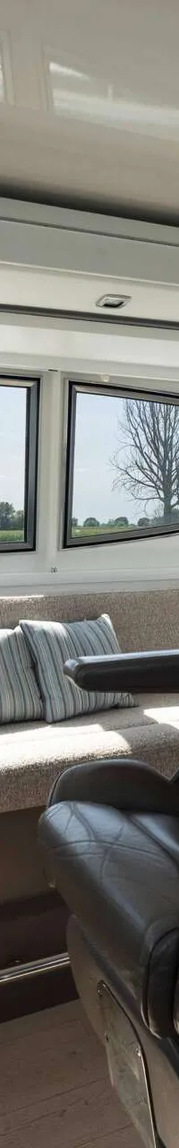 De foto toont het interieur van een stuurhuis met een stuurstand, een grijze kapiteinsstoel, een bankje en uitzicht naar…