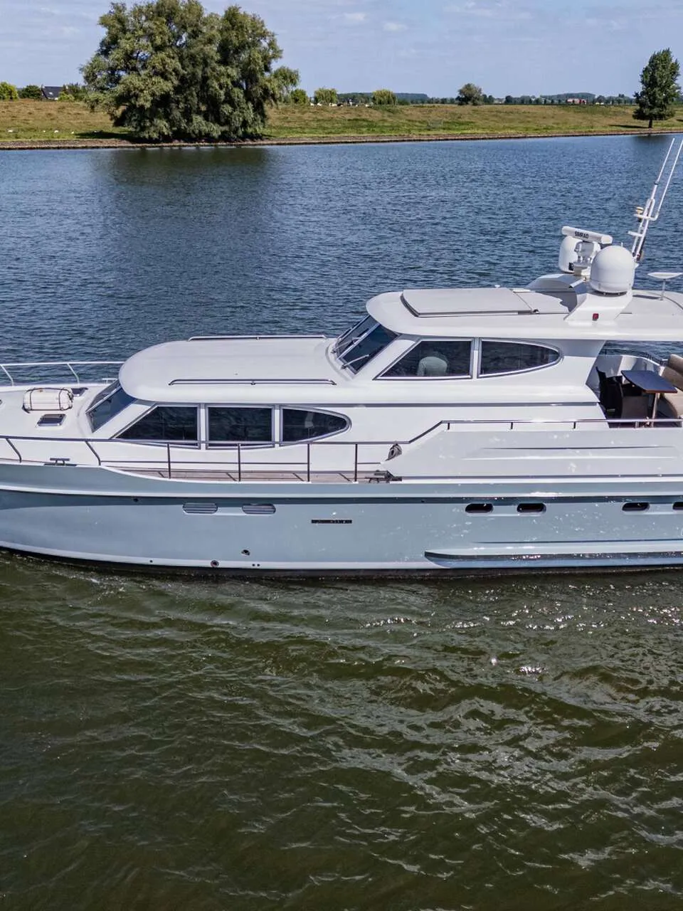 Een grijze motorboot vaart op een waterweg met een groene oever en bomen op de achtergrond. — Vripack 63 Custom M/Y