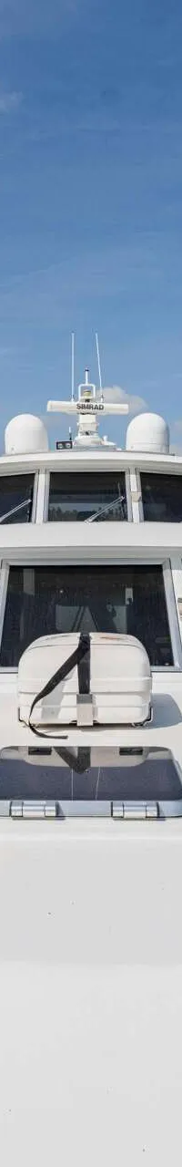Een witte motorboot vaart op een rivier met een brug en bomen op de achtergrond onder een blauwe lucht.