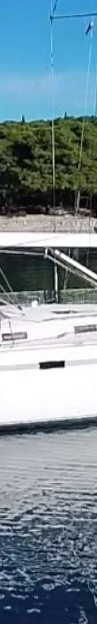 Een witte zeilboot met een grijze kap ligt op rustig water, met een beboste kustlijn op de achtergrond. — Bavaria 55 Cruiser
