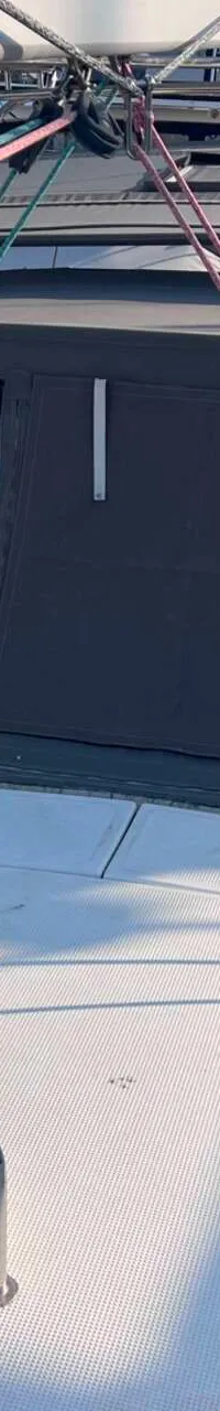 Een dek van een zeilboot met een grijze buiskap, lijnen en een mast in een haven. — Bavaria 55 Cruiser