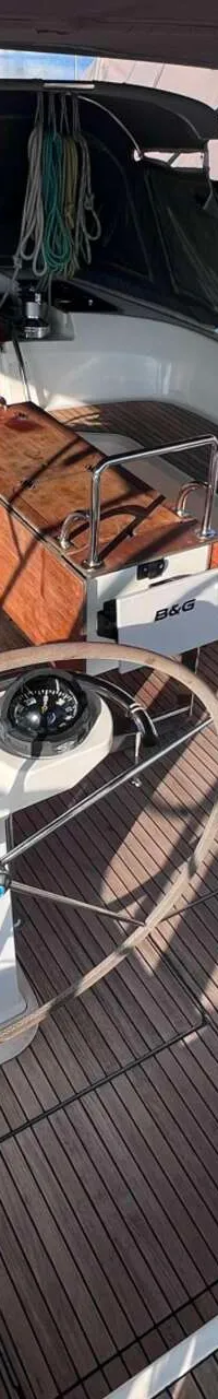 Een bovenaanzicht van de cockpit van een zeilboot met een houten dek, twee stuurwielen en een inklapbare tafel.