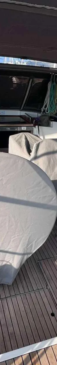 Een bovenaanzicht van de kuip van een zeilboot met een teakhouten dek, een tafel en twee stuurwielen afgedekt met grijze…
