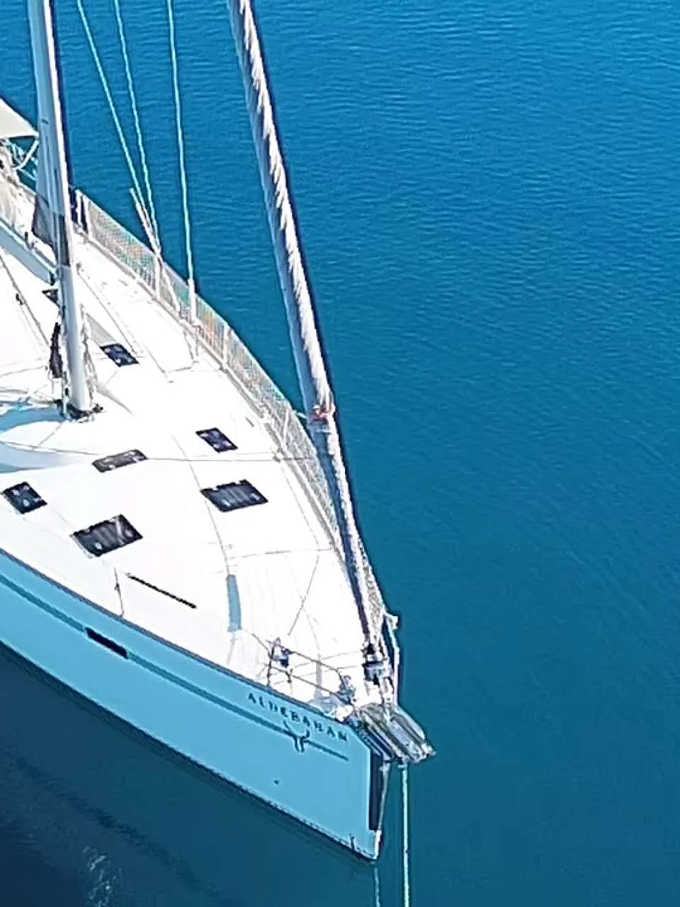 Een witte zeilboot met de naam "ALDEBARAN" ligt in helder blauw water, gezien vanaf de voorkant. — Bavaria 55 Cruiser