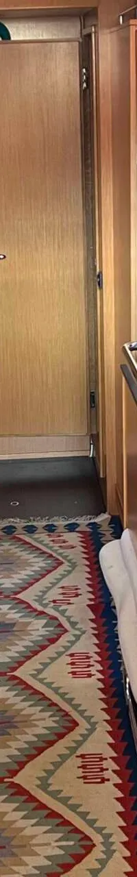 Een interieur van een boot met een houten tafel, banken, kasten, een keukenblok en een vloerkleed. — Bavaria 55 Cruiser