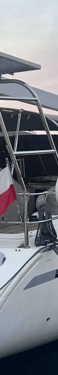 Een witte zeilboot met een Poolse vlag en een gele reddingsboei ligt aangemeerd in een haven. — Bavaria 55 Cruiser