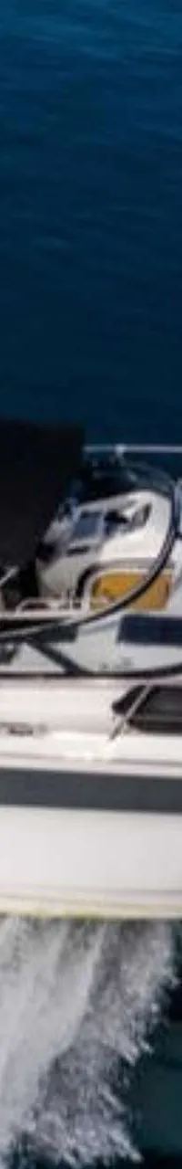 Een witte motorboot met een donkerbruin dek en een zwarte bimini vaart op blauw water, met een zonnepaneel op het dak.