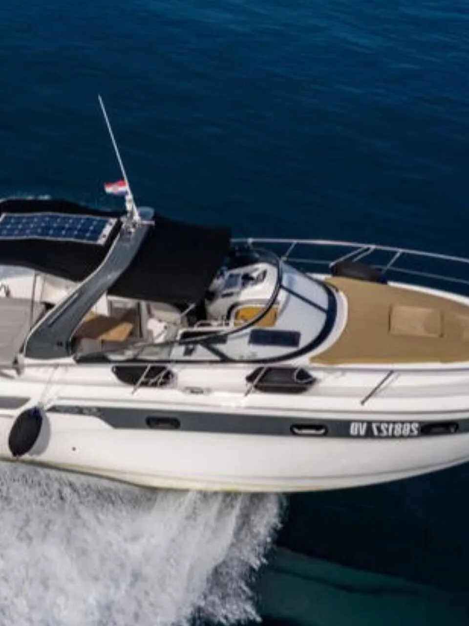 Een witte motorboot met een donkerbruin dek en een zwarte bimini vaart op blauw water, met een zonnepaneel op het dak.