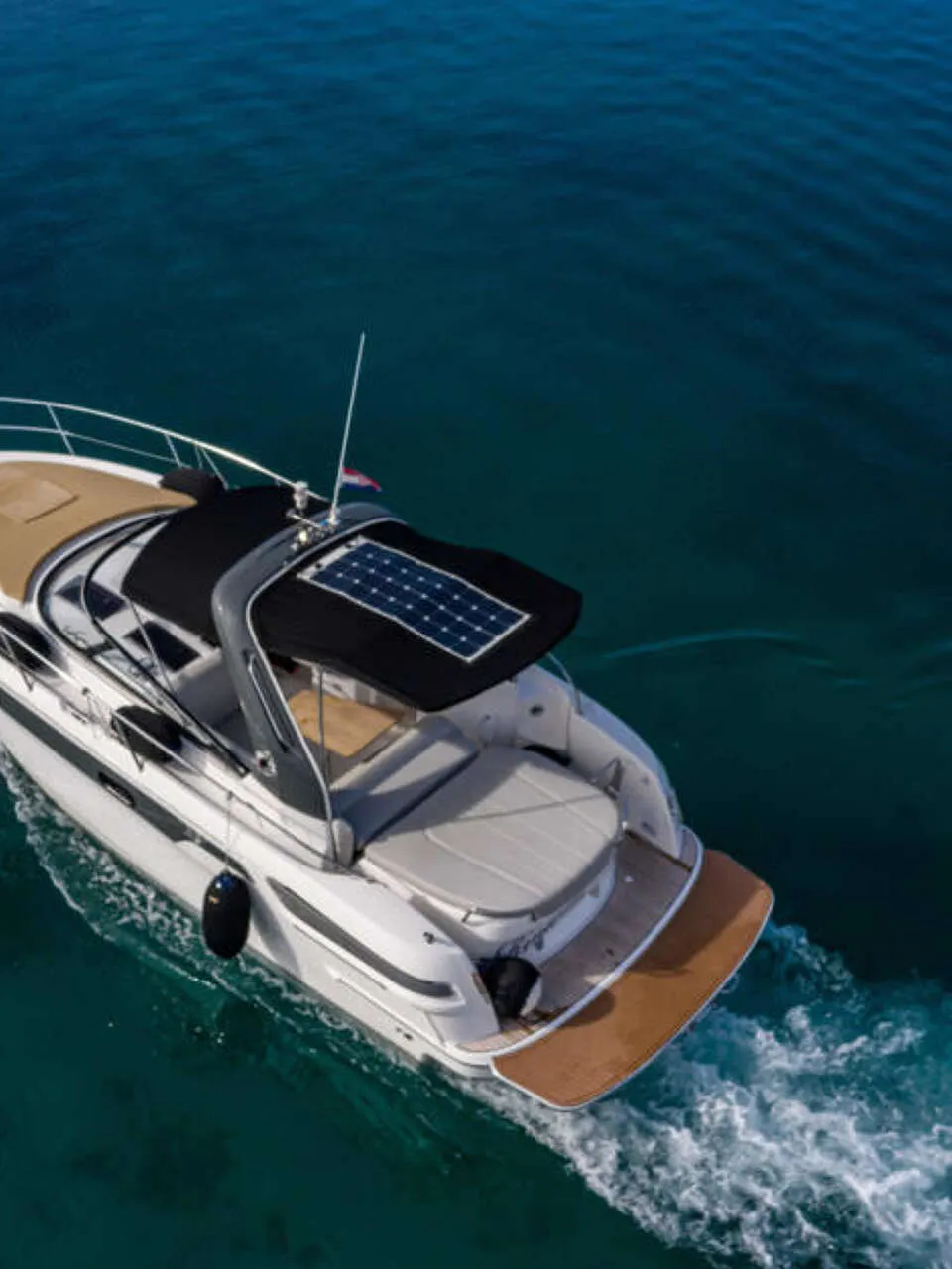 Een witte motorboot met een bruin dek en zwarte bimini met zonnepanelen vaart op blauw water. — Bavaria S29