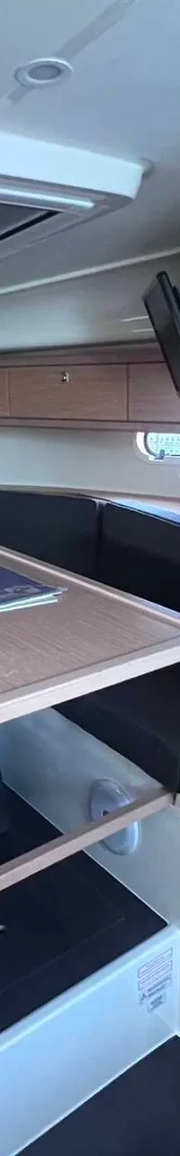 Een kajuit met een houten tafel, donkere banken, een televisie en een deur. — Bavaria S29