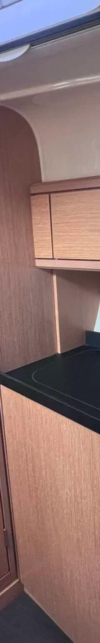 Een kombuis met een donker aanrechtblad, een spoelbak, een kraan, een kookplaat en houten kasten.