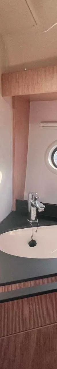 Een badkamer met een wastafel, spiegel, douchekop, patrijspoorten en houten kasten.