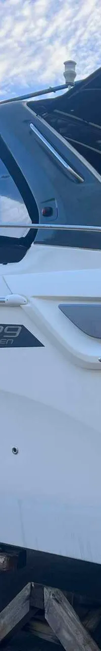 Een witte motorboot met een donkerblauwe kap staat op houten blokken op een betonnen ondergrond onder een bewolkte hemel.