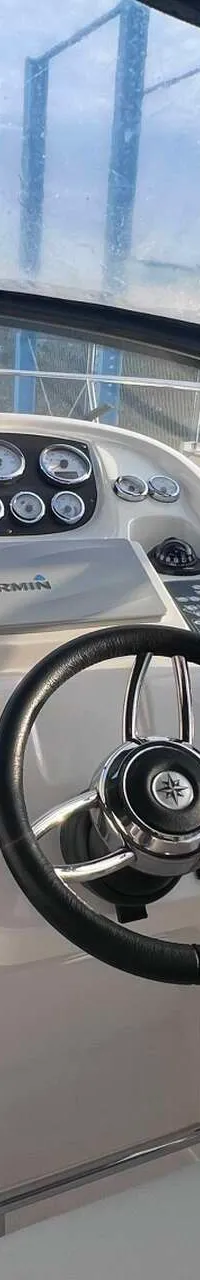 De foto toont de stuurstand van een boot met een stuurwiel, diverse meters, een Garmin-apparaat en een schuifdeur naar de…