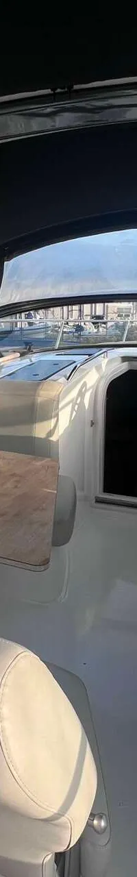 Een bootinterieur met een stuur, zitplaatsen, twee tafels en een zwarte biminitop.