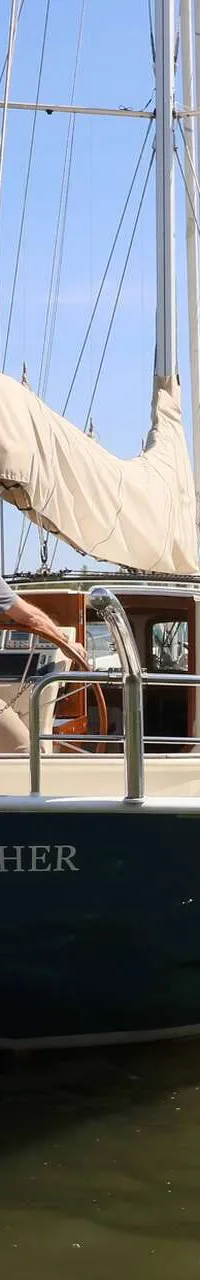 Een zeilboot met de naam "KINGFISHER" vaart op een meer met een persoon aan het roer en een Nederlandse vlag.