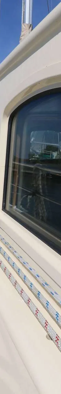 De foto toont de zijkant van een boot met ramen, een reling en touwen, met water en landschap op de achtergrond.