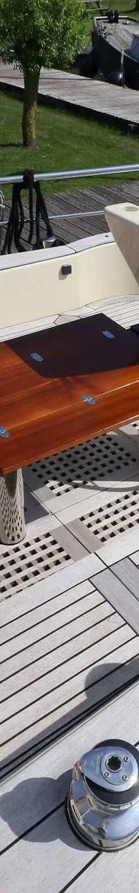 De foto toont het achterdek van een boot met een houten stuurwiel, een opklapbare houten tafel en een teakhouten dek.