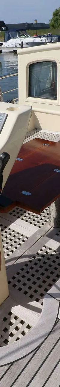 Een boot met een houten stuurwiel, een dashboard met meters en een houten kajuitingang, liggend in een haven.