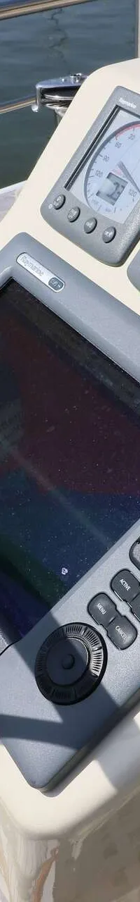 Een stuurstand met een houten stuurwiel, diverse Raymarine navigatie-instrumenten en een gashendel.