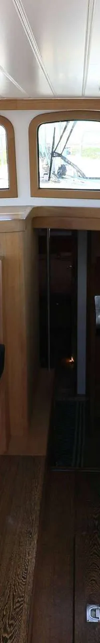 Een interieur van een boot met een houten tafel, zwarte banken, ramen met gordijnen en een stuurstand met een witte stoel.