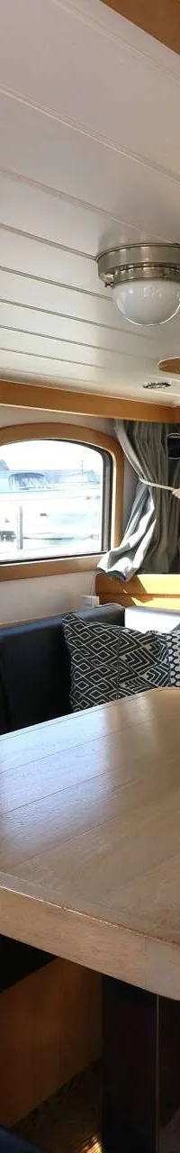 Een interieur van een boot met een houten tafel, zwarte banken, ramen met uitzicht op water en andere boten, en een wit…