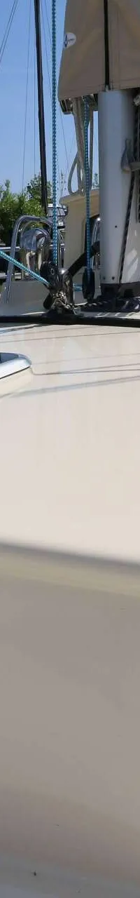 Een crèmekleurig dek van een zeilboot met een luik, mast en zeil, met een blauwe lijn en reling op de achtergrond.