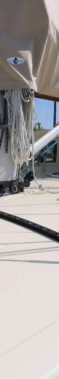 Een bovenaanzicht van het dek van een zeilboot met een opgerold zeil en mast, met een waterweg en groen gras op de…