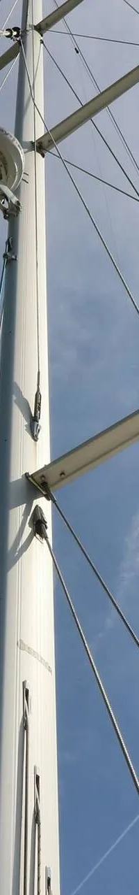 Een witte mast met zalingen en verstaging, gezien tegen een blauwe lucht met wolken.