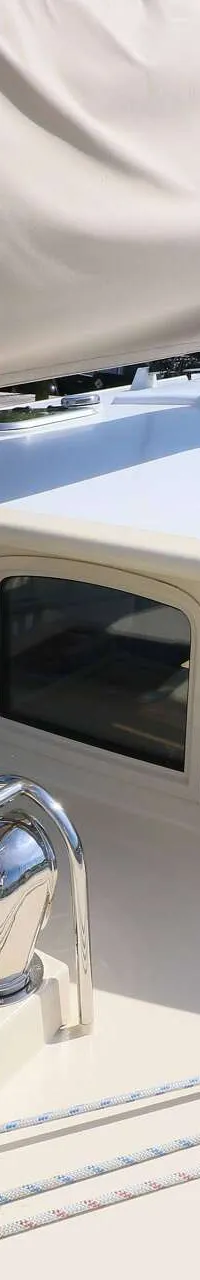 Een bovenaanzicht van het dek van een zeilboot met een beige zeilhoes, ramen in de kajuitopbouw en diverse lijnen.