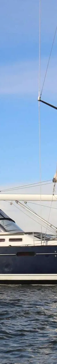 Een donkerblauwe zeilboot met een witte streep op de romp vaart op open water onder een blauwe lucht. — Beneteau 57