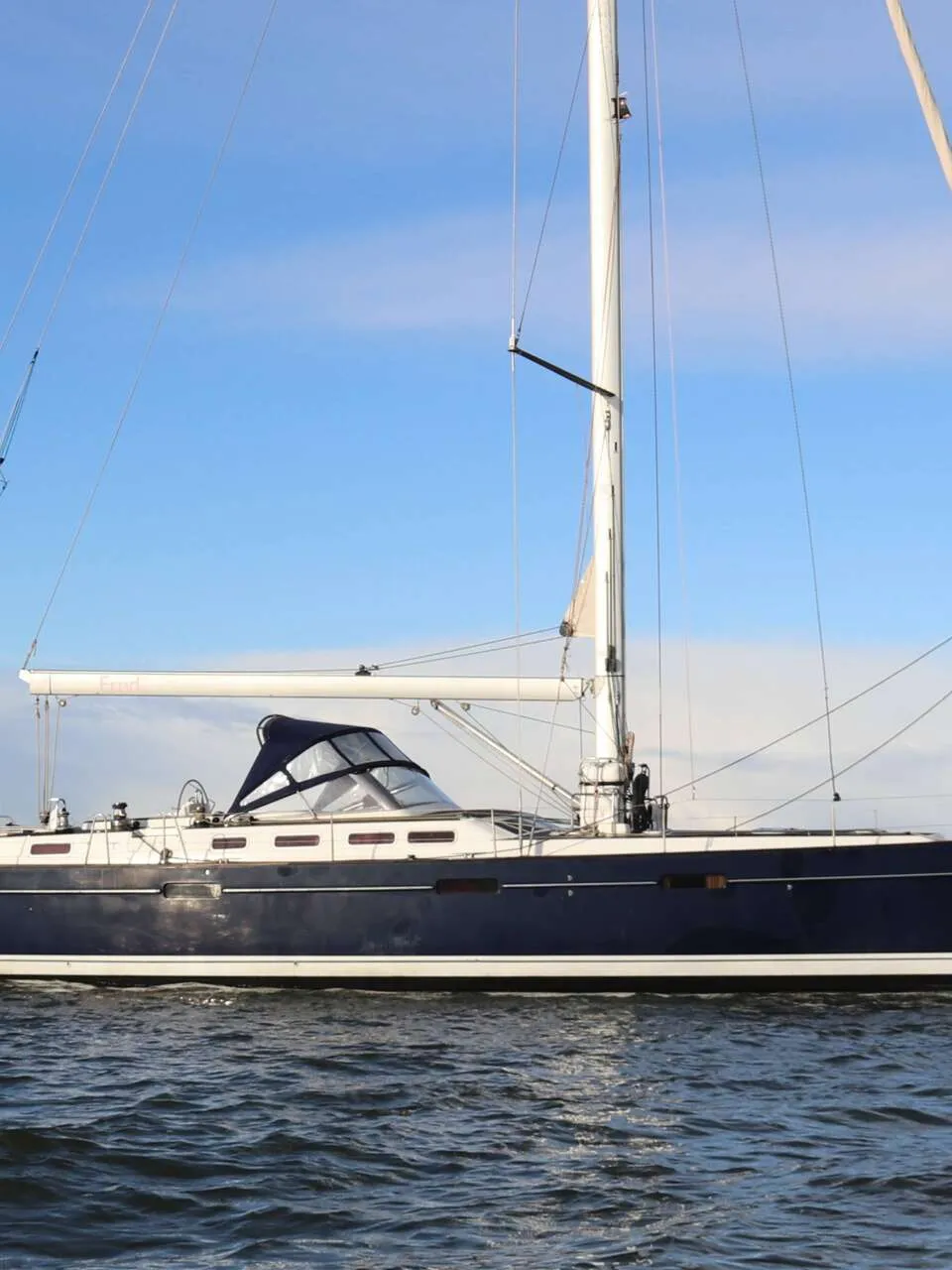 Een donkerblauwe zeilboot met een witte streep op de romp vaart op open water onder een blauwe lucht. — Beneteau 57