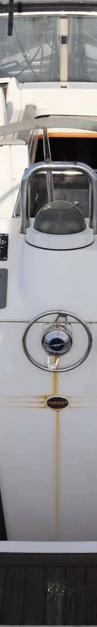 Een bovenaanzicht van de cockpit van een boot met een wit stuurwiel, instrumentenpaneel en houten dek. — Beneteau 57