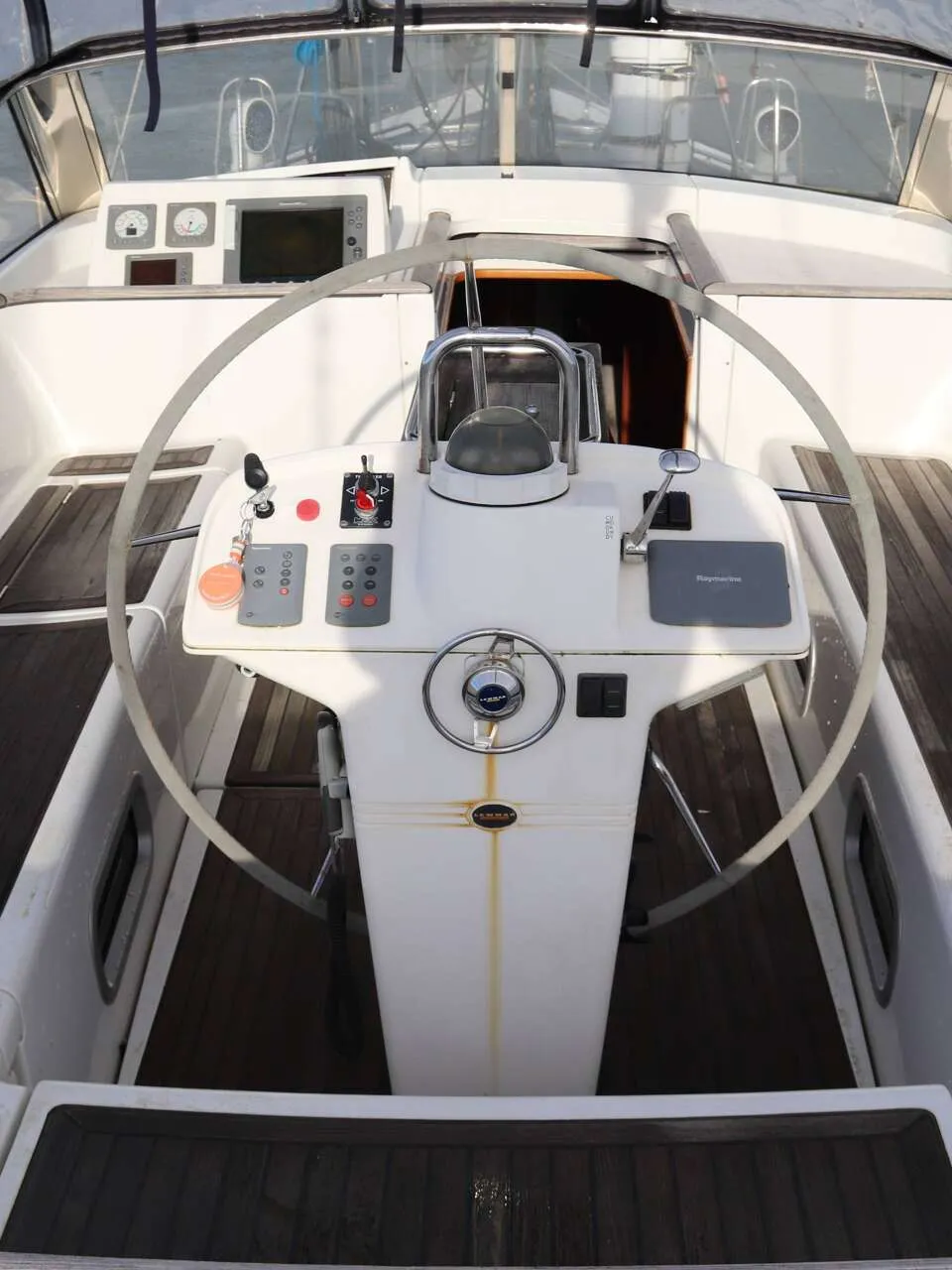 Een bovenaanzicht van de cockpit van een boot met een wit stuurwiel, instrumentenpaneel en houten dek. — Beneteau 57