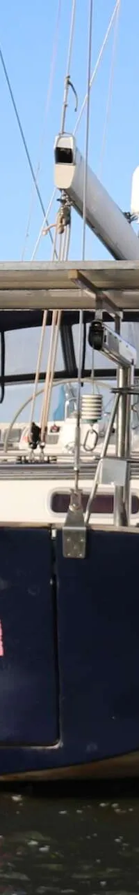 Een donkerblauwe zeilboot met de naam "Fred" in roze letters op de spiegel, ligt in het water. — Beneteau 57