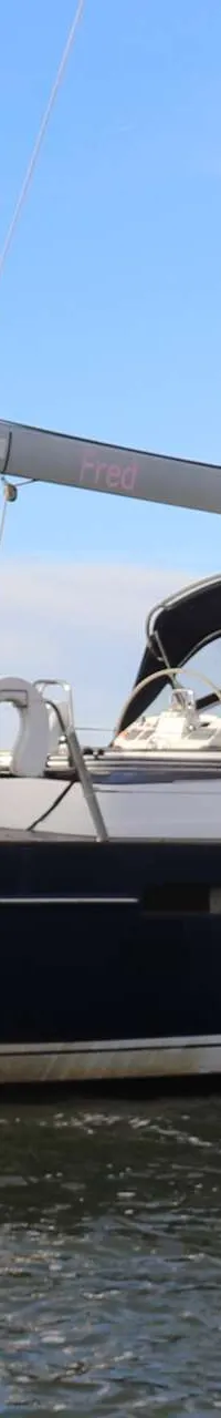 Een donkerblauwe zeilboot met de naam "Fred" op de spiegel, drijft op water onder een blauwe lucht. — Beneteau 57