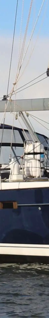Een blauw-witte zeilboot met de naam "Fred" op de giek vaart op water met windmolens op de achtergrond. — Beneteau 57
