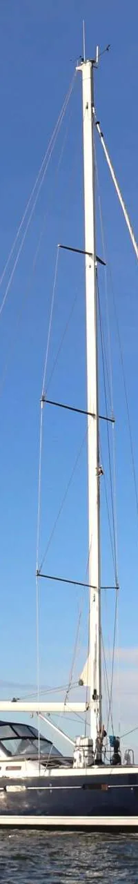 Een donkerblauwe zeilboot met witte mast en opgerolde zeilen drijft op rustig water onder een helderblauwe lucht.