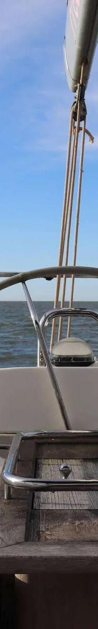 Een stuurwiel en houten tafel op een boot met de zee en een blauwe lucht op de achtergrond. — Beneteau 57