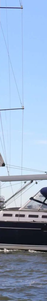 Een donkerblauwe zeilboot vaart op water met een vuurtoren en gebouwen op de achtergrond. — Beneteau 57