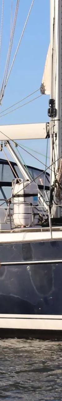 Een donkerblauwe zeilboot met witte strepen vaart op het water onder een helderblauwe lucht. — Beneteau 57