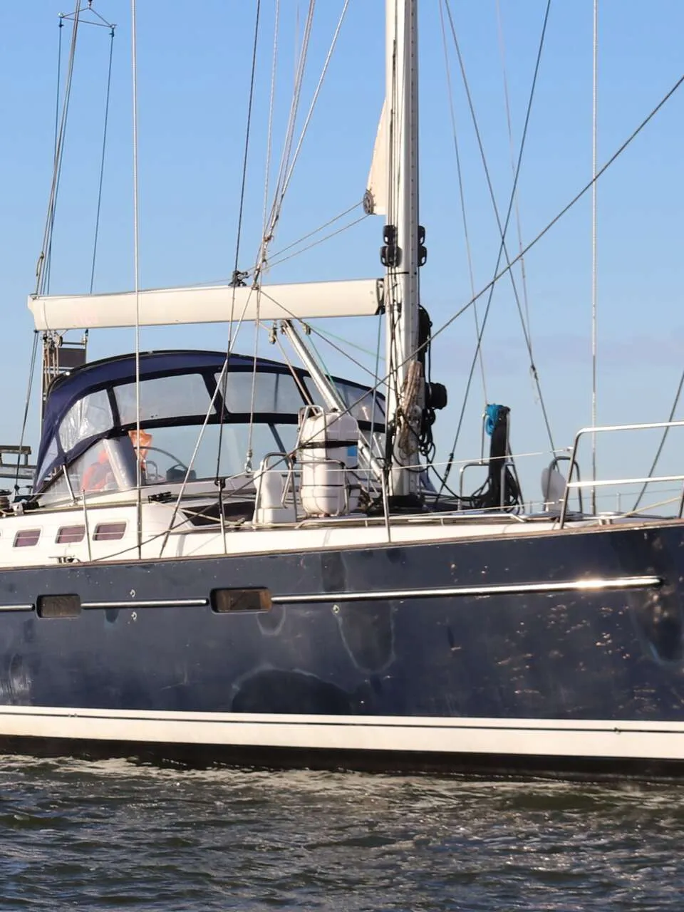 Een donkerblauwe zeilboot met witte strepen vaart op het water onder een helderblauwe lucht. — Beneteau 57