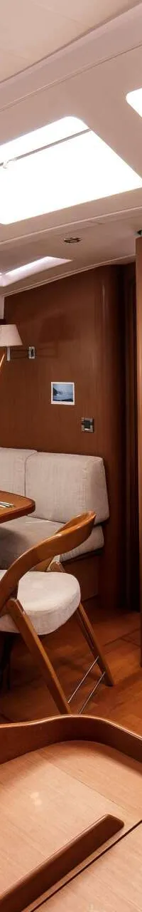De foto toont een interieur van een boot met een houten vloer, een eettafel met servies, banken en een televisie.